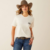 Woman wearing a light t-shirt with ariat brand logo, blue jeans, and a brown western hat on a beige background